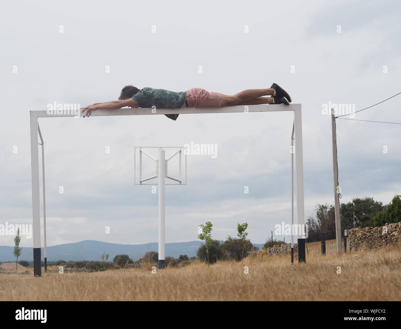La longitud total del hombre descansando sobre la meta de fútbol en campo de hierba contra el cielo nublado Foto de stock