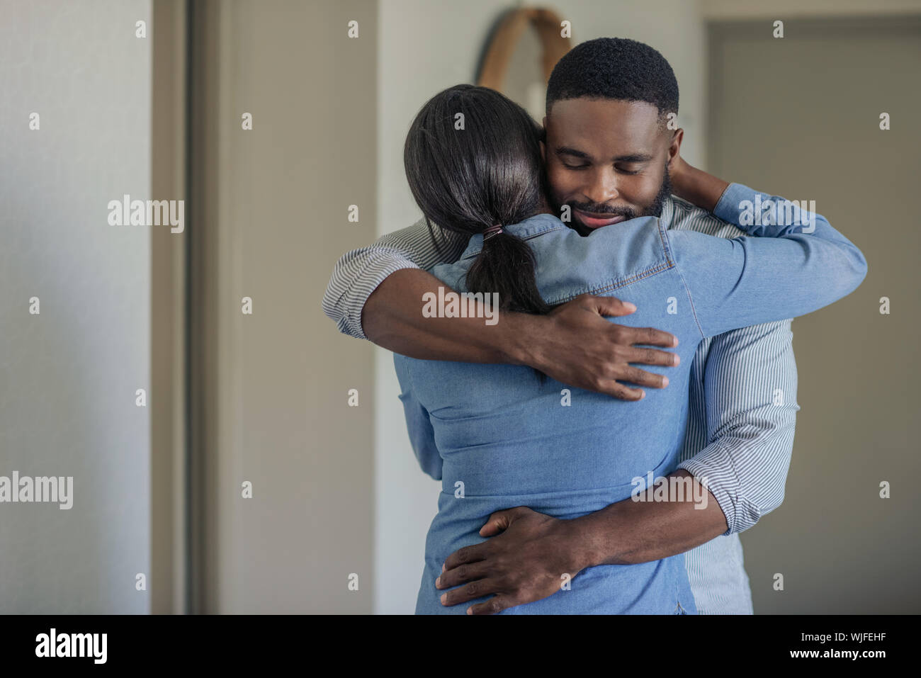 Afectuoso joven hombre afroamericano abrazando a su esposa en el hogar Foto de stock