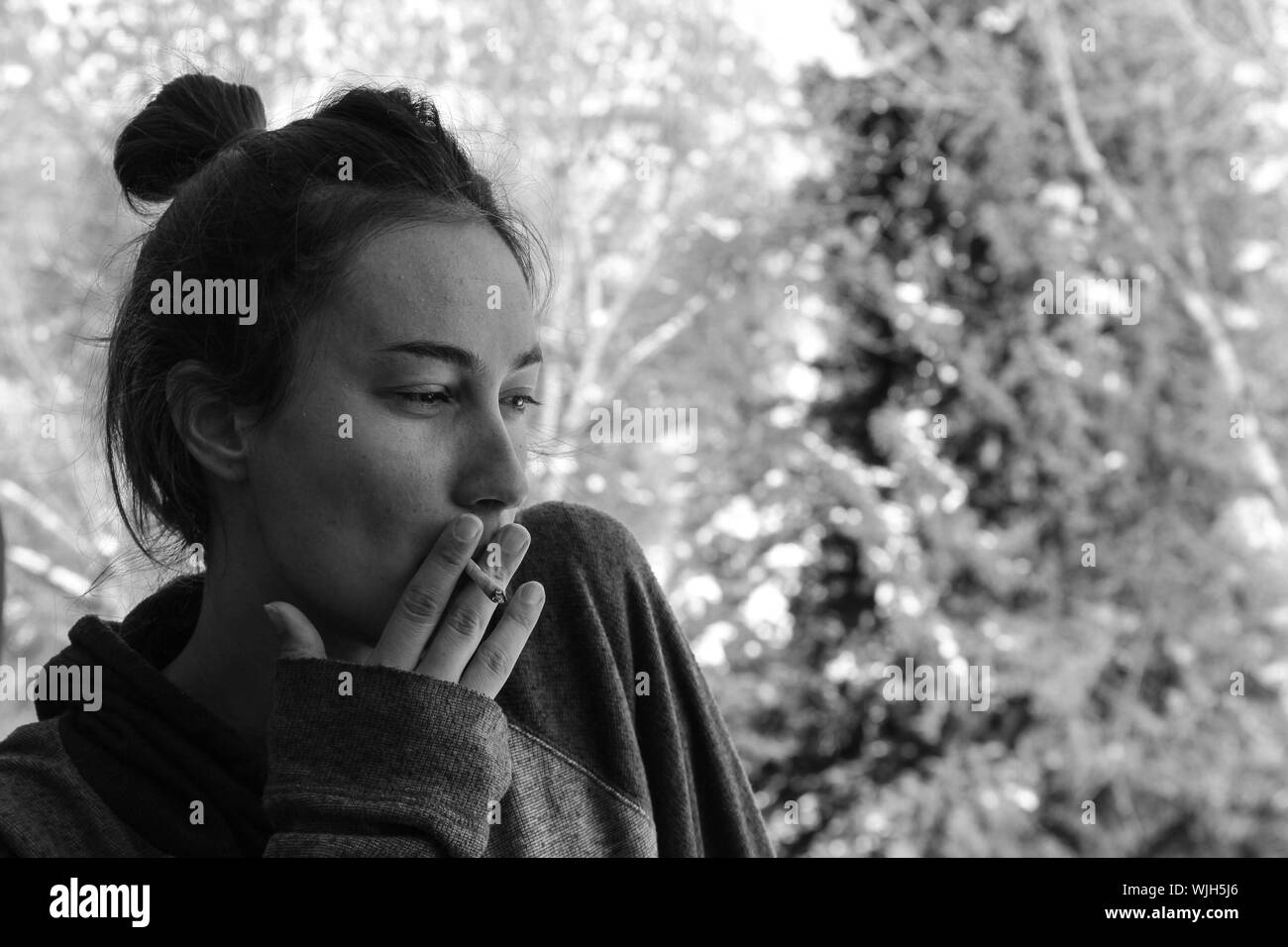 Close-up de reflexivo Joven fumar cigarrillo contra árboles Foto de stock