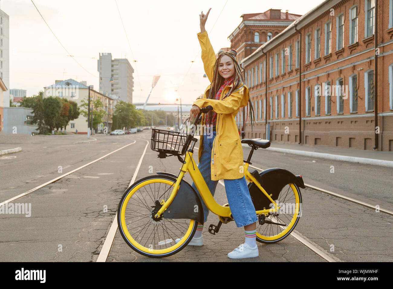 Mujer joven vistiendo abrigo color amarillo y pigtails, montando en bicicleta en la ciudad. Foto de stock