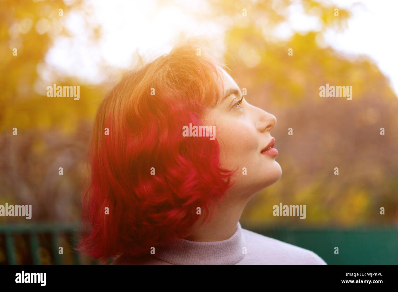 Mujer hermosa con el cabello teñido de color rojo y fondo de otoño de hojas amarillas. Foto de stock