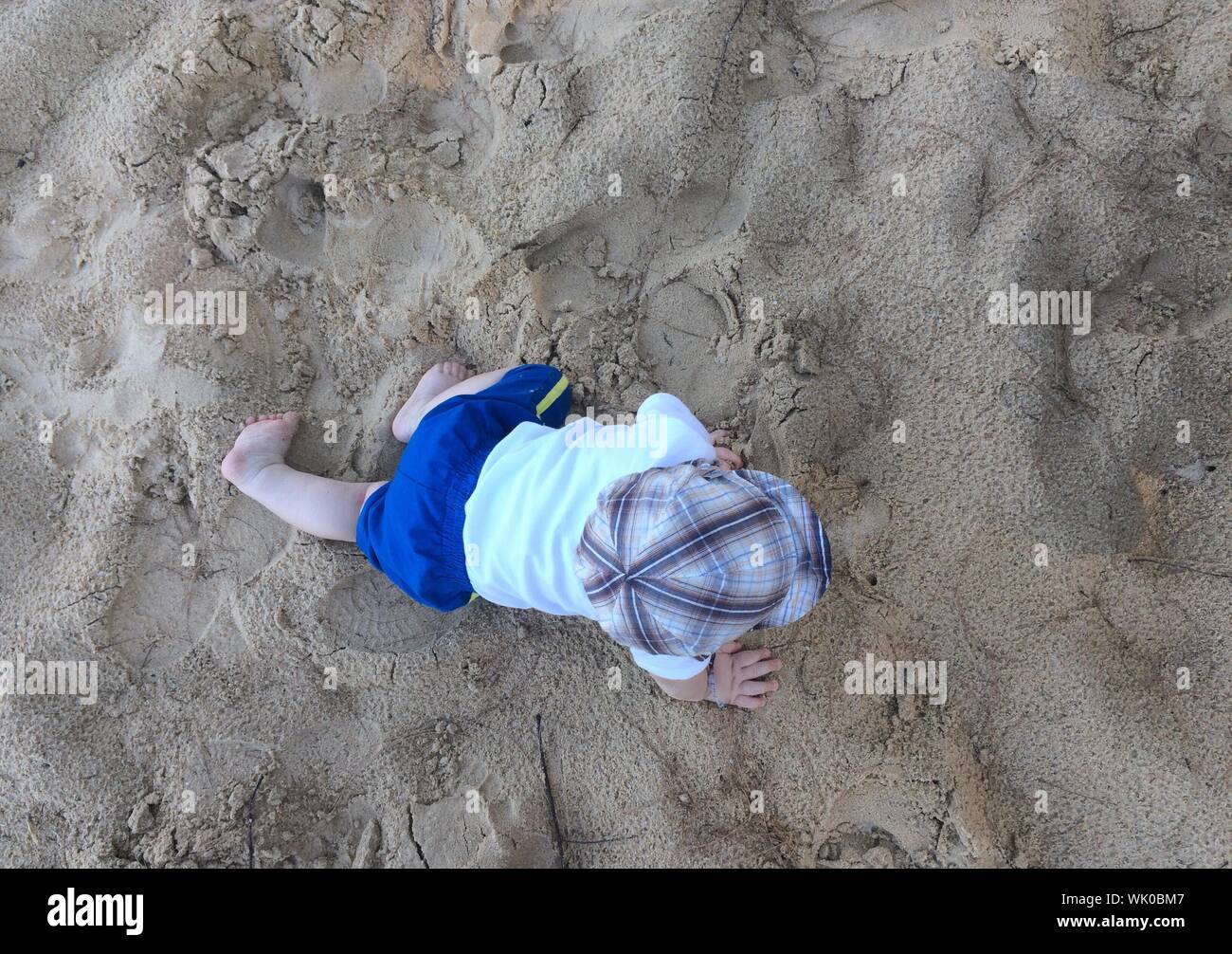 Directamente encima de la vista de Baby Boy arrastrándose sobre la arena en la playa Foto de stock