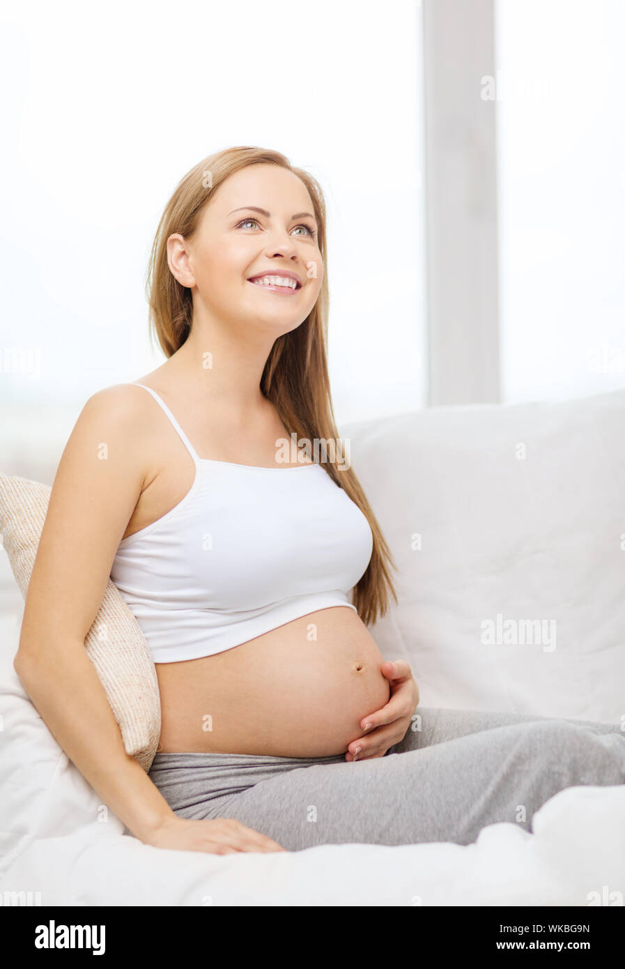 El embarazo, la maternidad y el concepto de la felicidad - feliz mujer embarazada sentada en el sofá y tocar su vientre y soñar Fotografía de stock Alamy