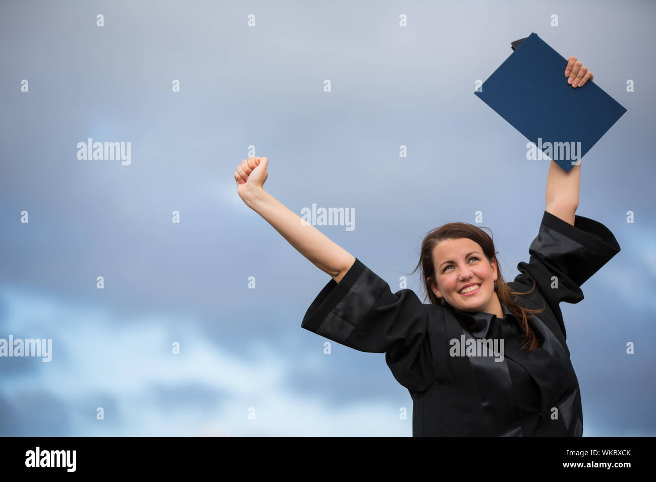 Bastante joven, celebrando con alegría su graduación - difusión amplia sus brazos, sosteniendo su diploma, saboreando su éxito (la imagen en tonos de color; shal Foto de stock