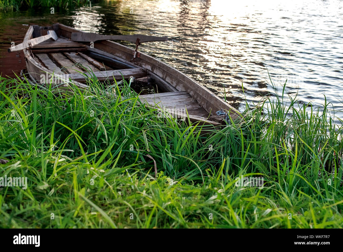 Un pequeño bote a remo de madera con una fractura en la parte inferior de un tranquilo lago cerca de la orilla. Bielorrusia Foto de stock