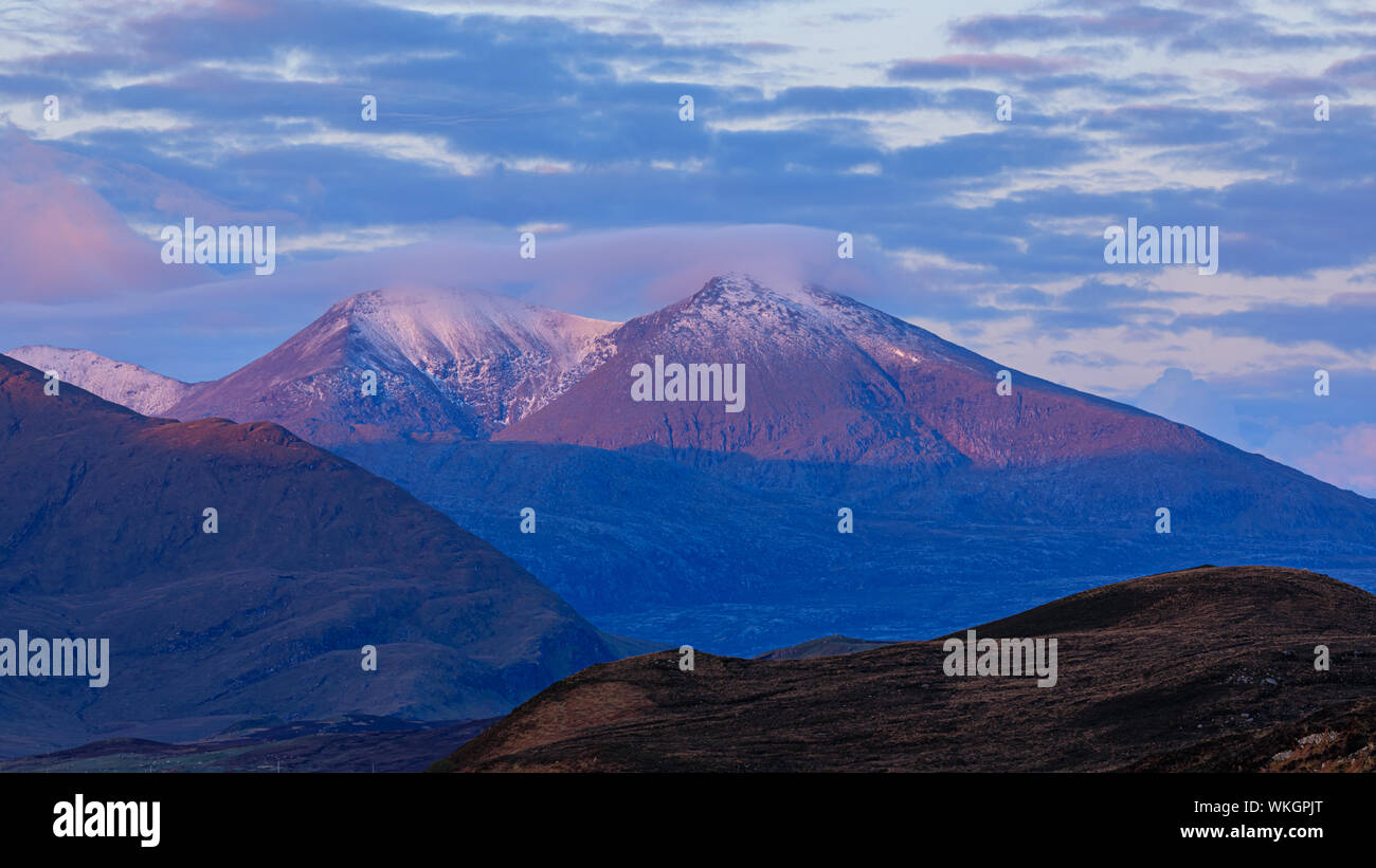 La montaña Beinn Spionnaidh Durness cercano al amanecer. Snow-capped e iluminado por el sol con luz rosa y azul del cielo detrás. Foto de stock