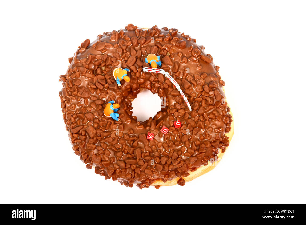 Imagen conceptual de una figura en miniatura de obreros se situó en un donut de chocolate mirando hacia abajo por el orificio central Foto de stock