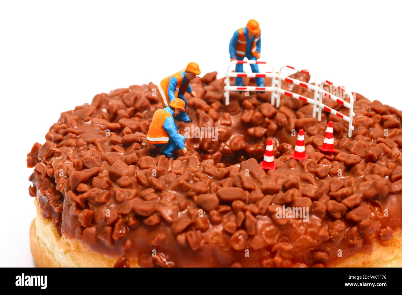 Imagen conceptual de una figura en miniatura de obreros se situó en un donut de chocolate mirando hacia abajo por el orificio central Foto de stock