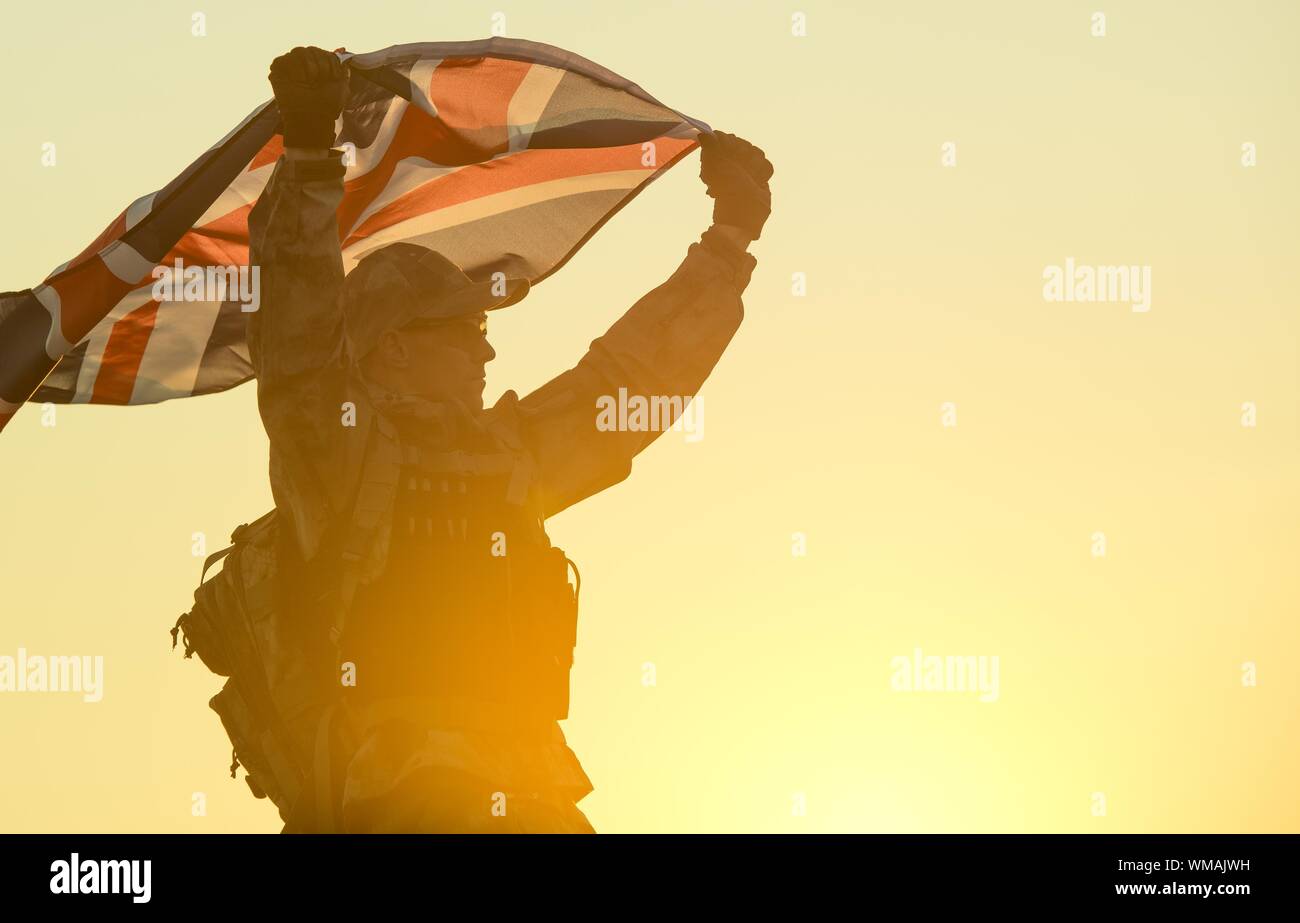 Ángulo de visión baja de soldado sosteniendo la bandera británica contra el cielo despejado durante la puesta de sol Foto de stock