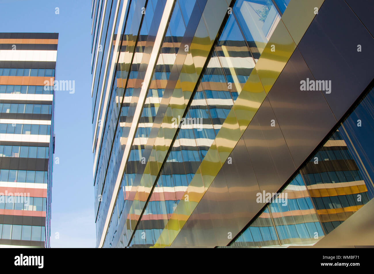 Moderna fachada de los edificios con líneas, colores y modelo reflejado en una pared de vidrio contra el cielo azul Foto de stock