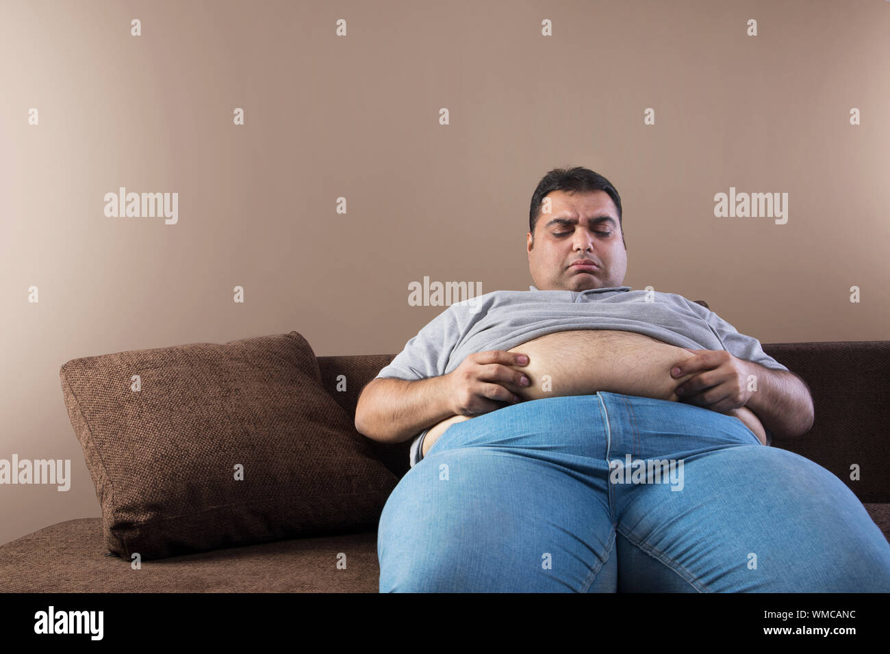 Obesos infeliz hombre sentado en el sofá sosteniendo su vientre grasa con  ambas manos Fotografía de stock - Alamy