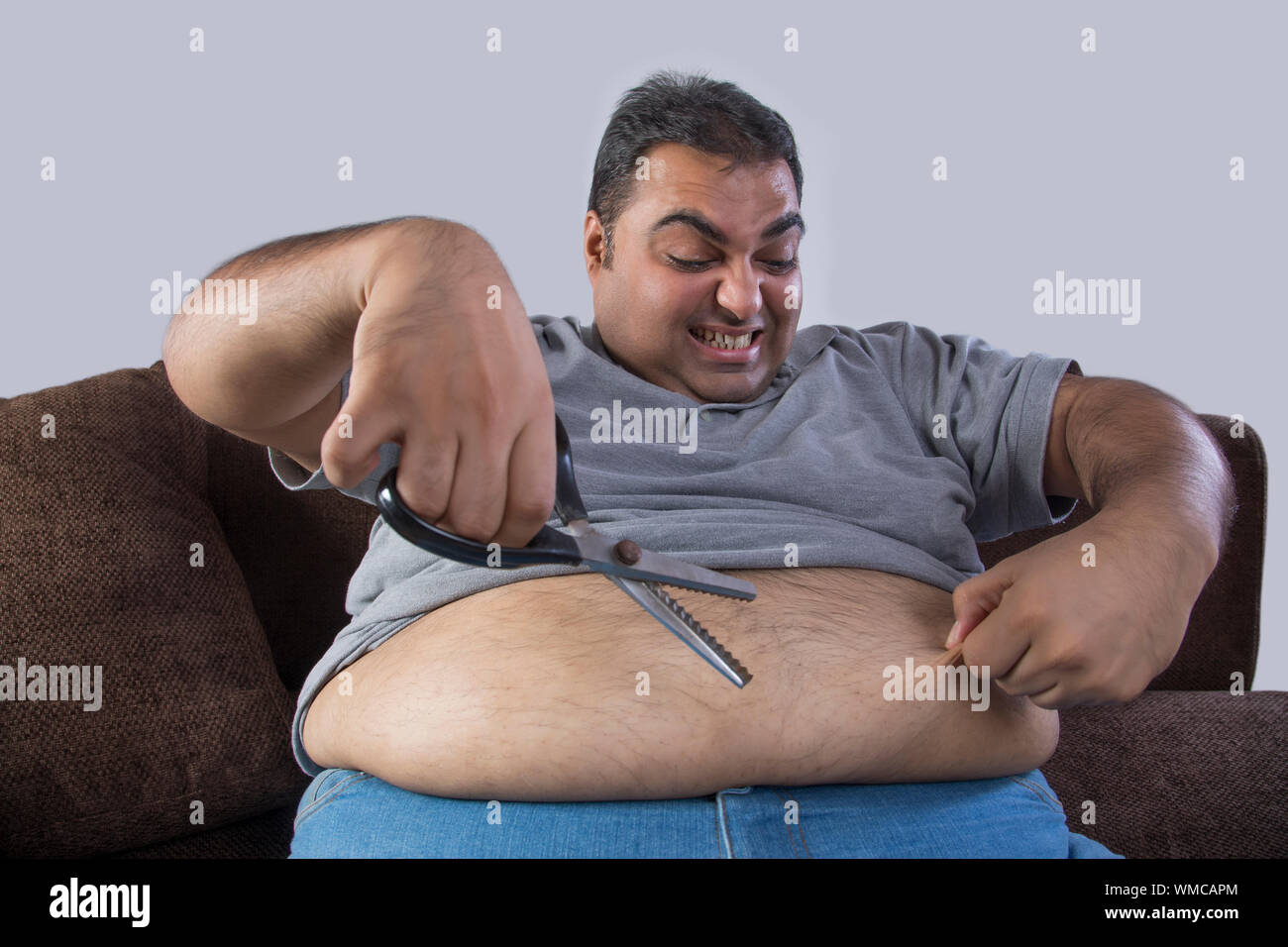 Obeso hombre con tijeras en una mano y la grasa del vientre en otros con intención de cortar el exceso de grasa Foto de stock