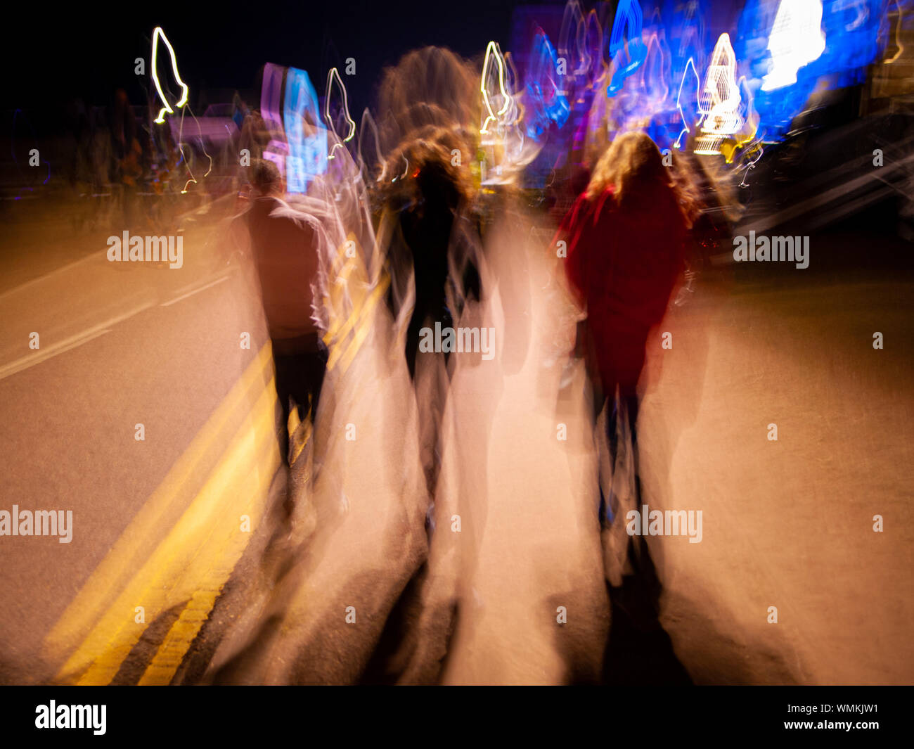 Tres personas caminando en la noche con el desenfoque de movimiento. Foto de stock