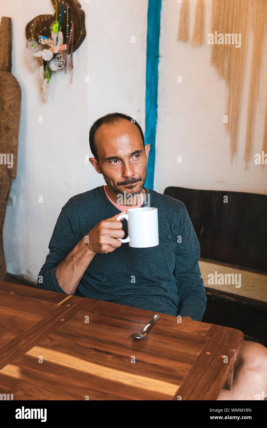 Edad media hispana apartar la mirada masculina con una taza de café en su mano Foto de stock