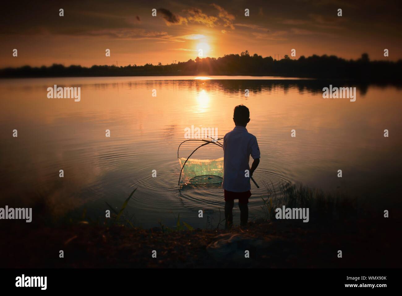 Vista trasera del Adolescente la pesca en Lakeshore durante la puesta de sol Foto de stock