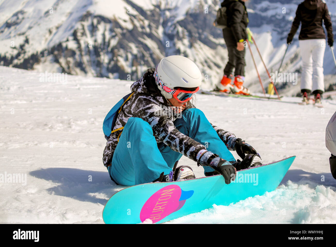 Lady snowboarder se sienta en la nieve y establece sus vínculos en un día soleado en Rochebrune / Megeve de los Alpes franceses. Esquiadores con vistas a los Alpes. Chamonix. Foto de stock