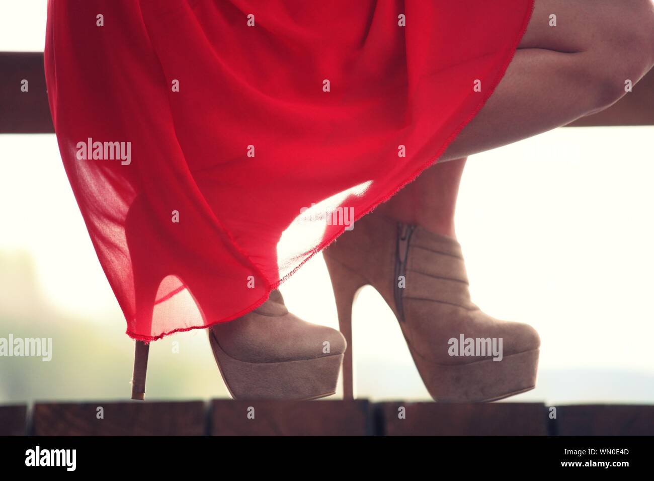 Bajo la sección de la mujer en el vestido rojo usar zapatos de tacón alto  en cuclillas sobre madera Fotografía de stock - Alamy