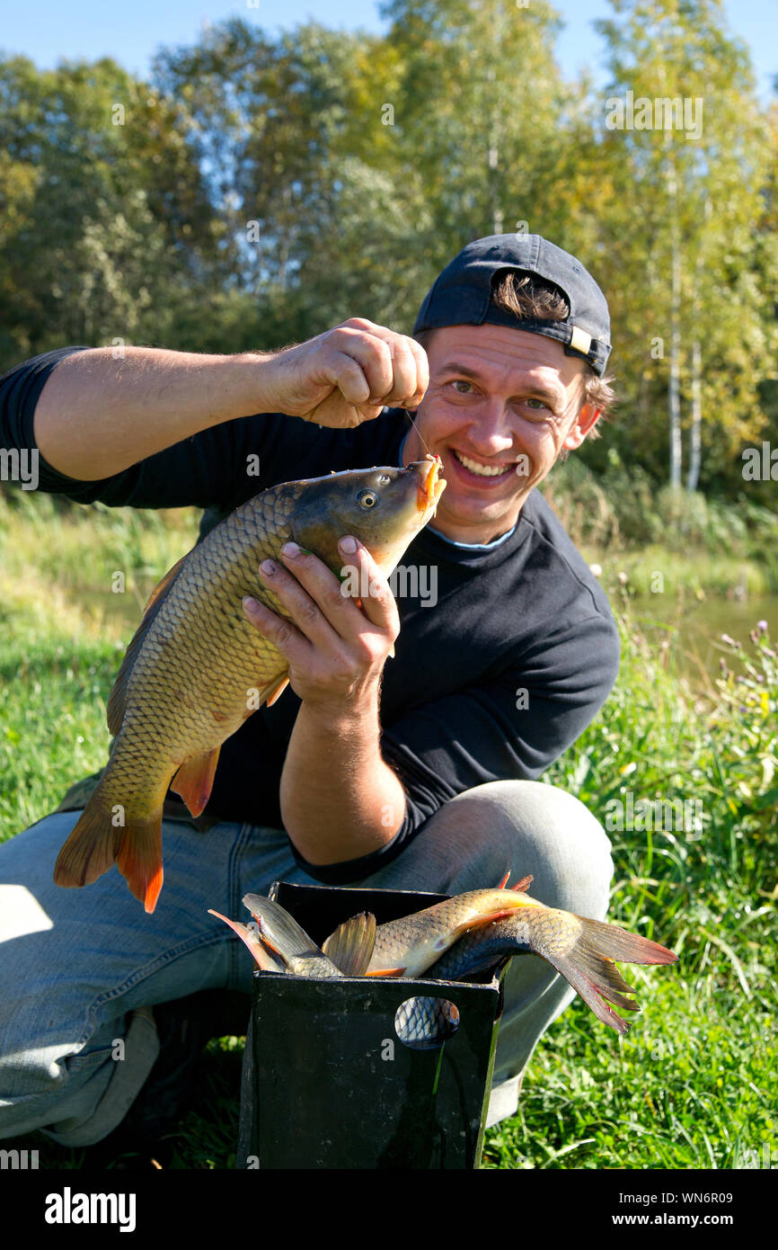 Retrato del hombre maduro sonriente sosteniendo los peces, mientras en cuclillas sobre césped Foto de stock