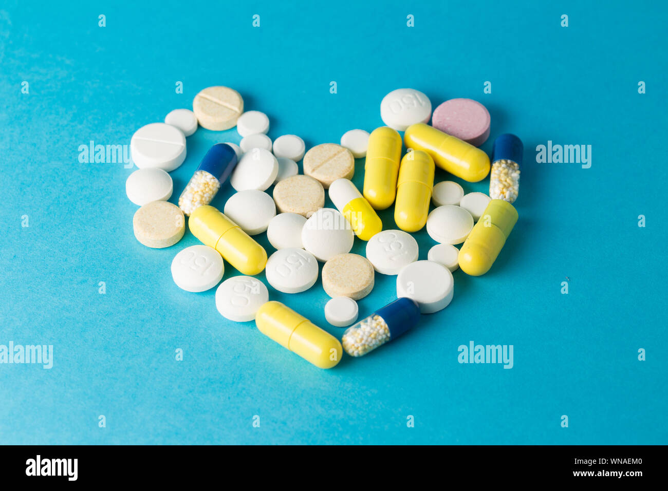 Medicamentos blanco, amarillo, azul redonda píldoras en forma de corazón sobre fondo azul. Foto de stock