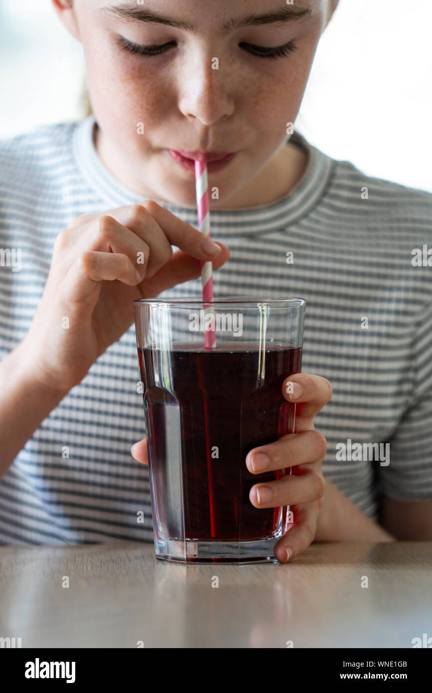 Chica bebiendo gaseosas azucaradas Soda de cristal con paja Foto de stock