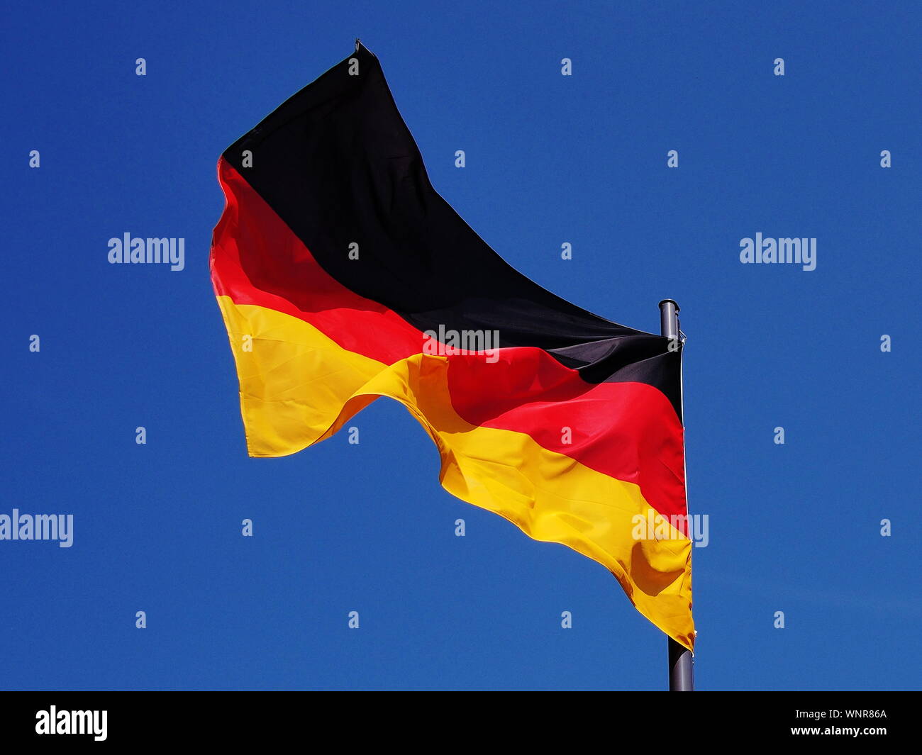 Bandera Alemana en gusty condiciones de viento bajo un cielo azul Foto de stock