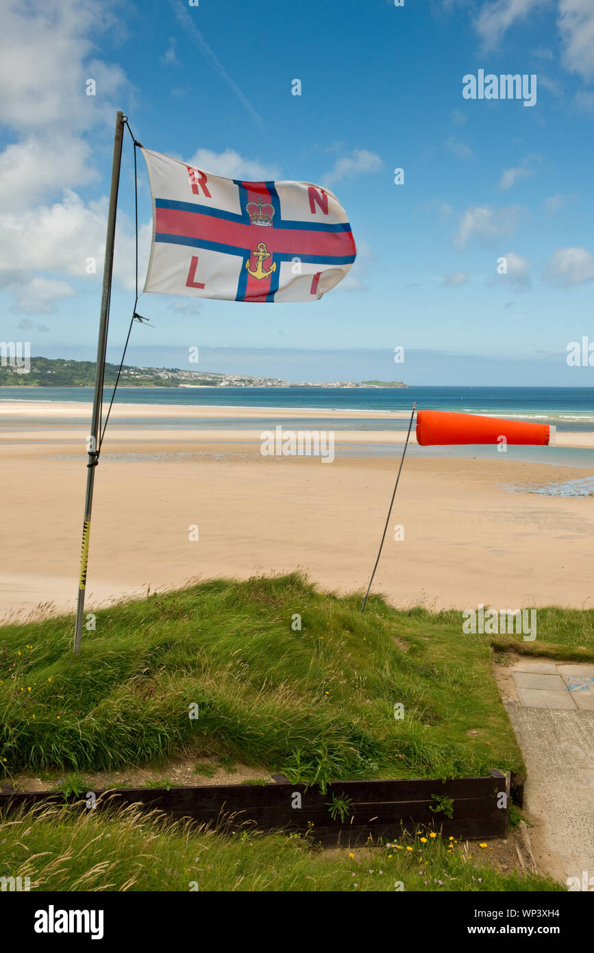 RNLI bandera ondeando en la brisa fuerte encima Hayle Playa. St Ives, Cornwall, Inglaterra, Reino Unido. Foto de stock