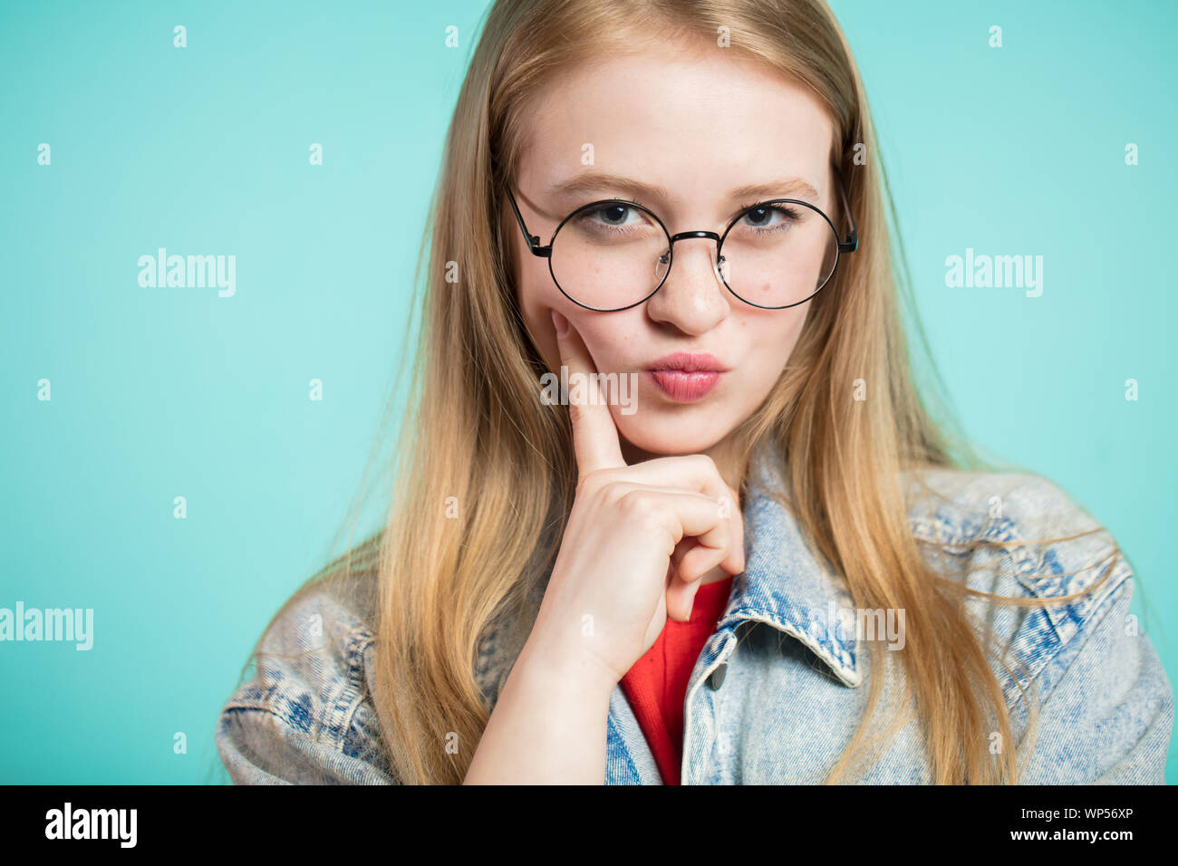 Chica guapa con gafas está determinada y el pensamiento mira la cámara  sobre fondo azul mirada penetrante Fotografía de stock - Alamy