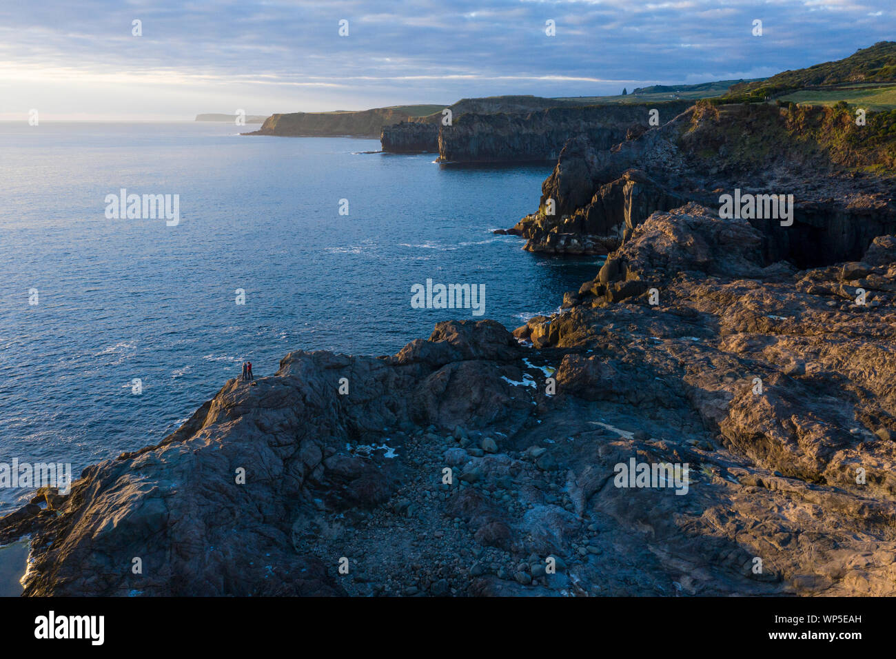 Dos fotógrafos tomar imágenes del amanecer en la rocosa costa de Ponta do Mistério en la isla Terceira, en las Azores. La luz de la mañana hits gi Foto de stock