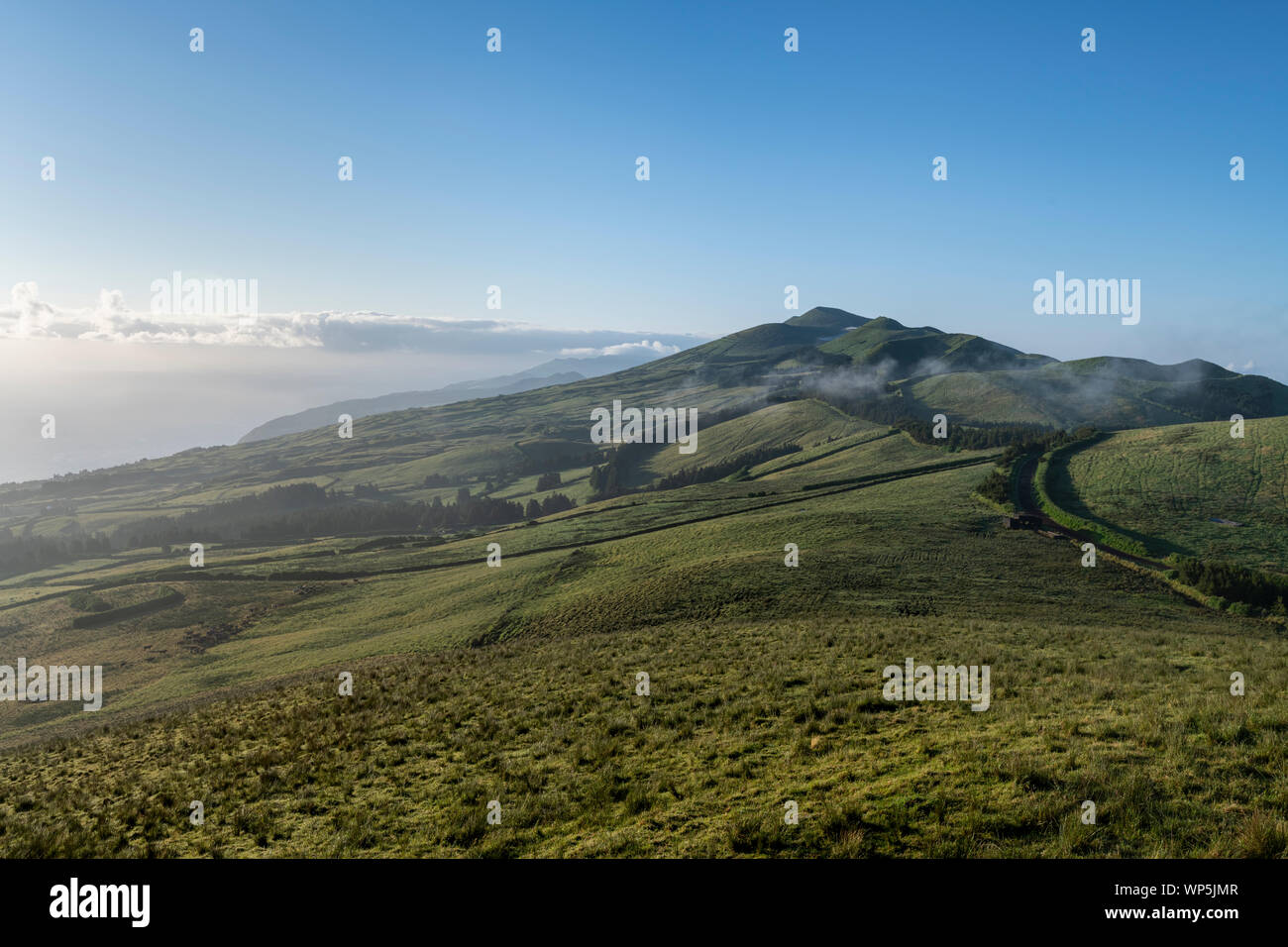 Temprano en la mañana la vista horizontal con el amanecer y la niebla sobre los verdes campos en la costa norte de la isla de Azores Sao Jorge, visto desde la central m Foto de stock