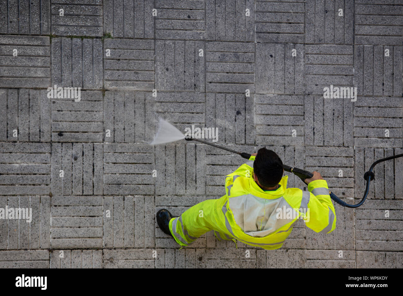 Vista superior de un trabajador de la limpieza de la acera de la calle con el chorro de agua de alta presión. Concepto de mantenimiento público Foto de stock