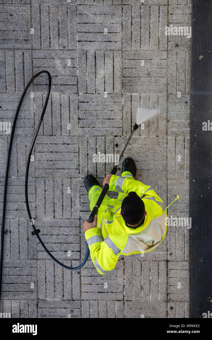 Vista superior de un trabajador de la limpieza de la acera de la calle con el chorro de agua de alta presión. Concepto de mantenimiento público Foto de stock