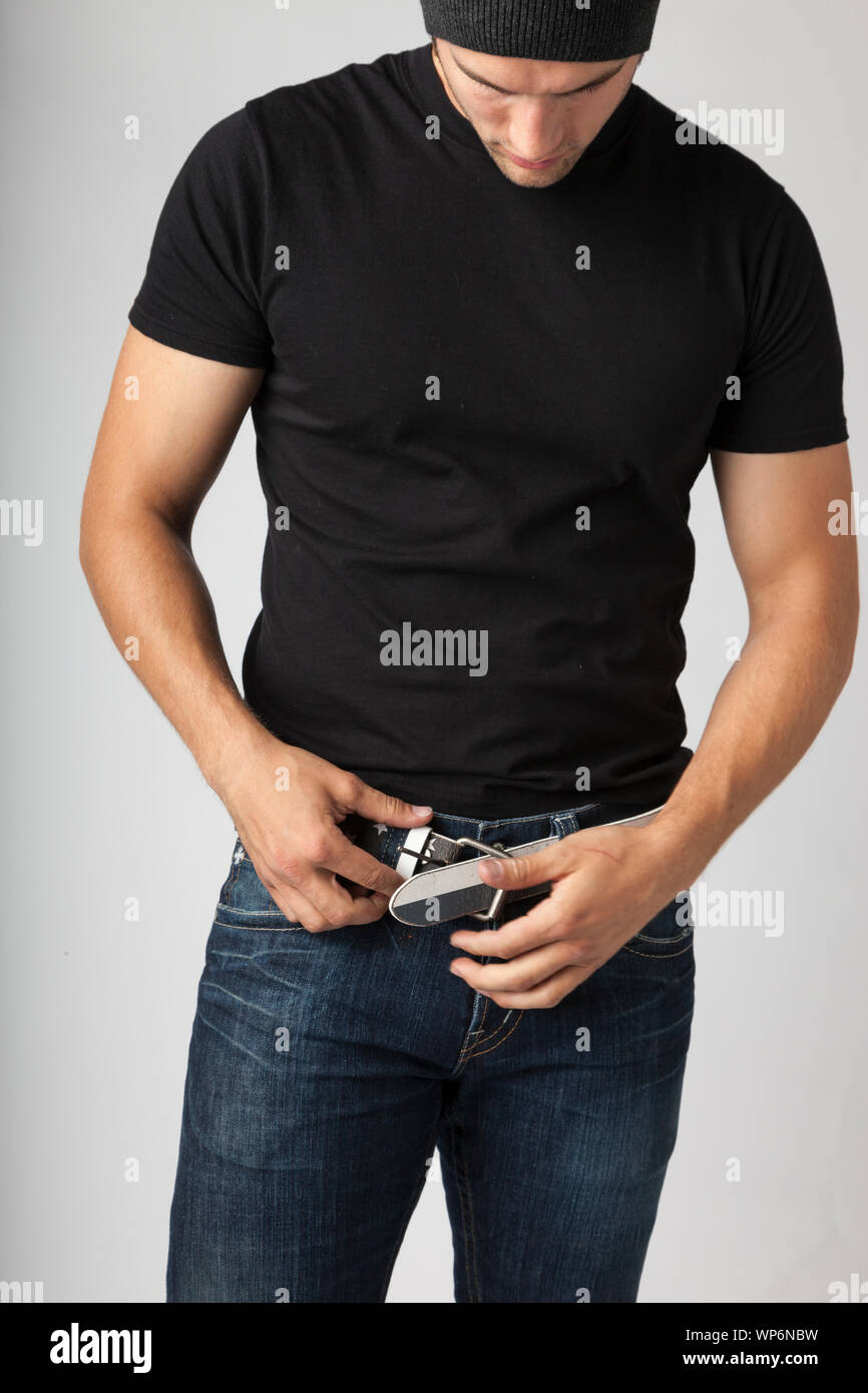 Hombre vestido con camiseta negra, vaqueros y jersey poniendo en un cinturón de hebilla de sujeción. Los hombres jóvenes del moderno estilos de moda ropa casual Fotografía de stock - Alamy