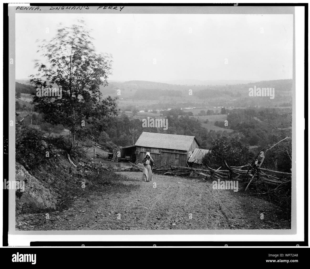 Paisaje con mujer caminar cuesta arriba, abajo, granero y rampa valla a lo largo de carreteras, en el crepúsculo, Dingman's Ferry, Pennsylvania Foto de stock