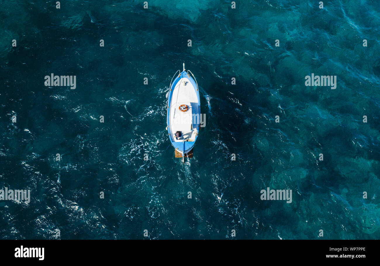Vista desde arriba, la impresionante vista aérea de un hermoso barco de pesca con un pescador a bordo navegando en un mar azul. La costa de Amalfi, Italia. Foto de stock