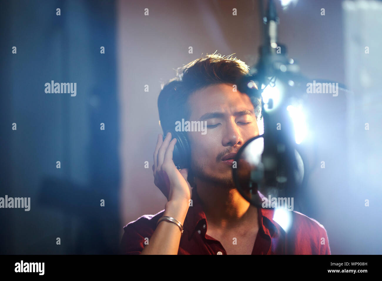Joven músico asiático cantante cantando la canción en estudio de grabación Foto de stock
