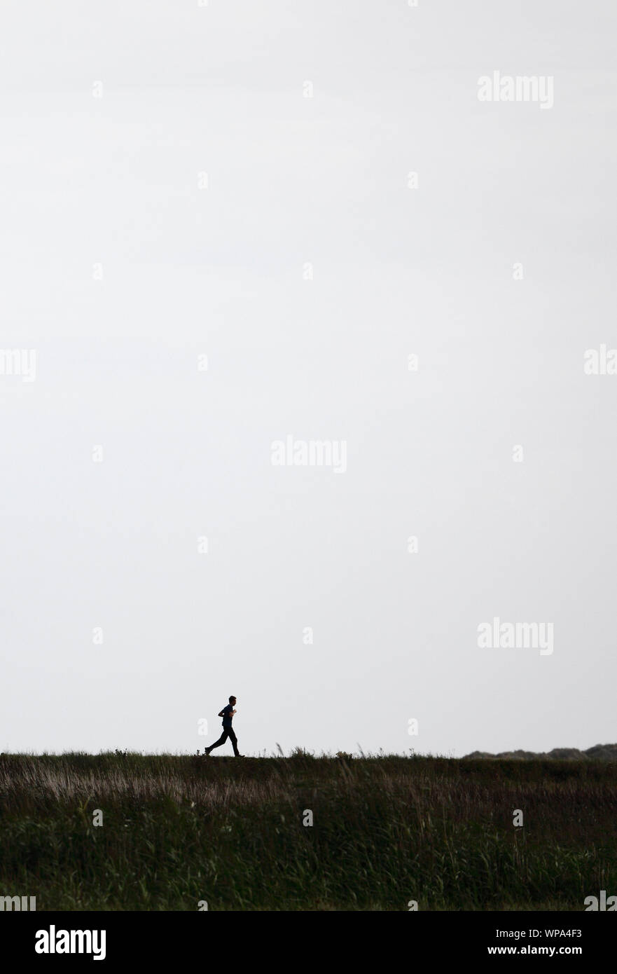 Joven hombre corriendo en la parte superior de un banco en los pantanos del norte de Norfolk. Foto de stock
