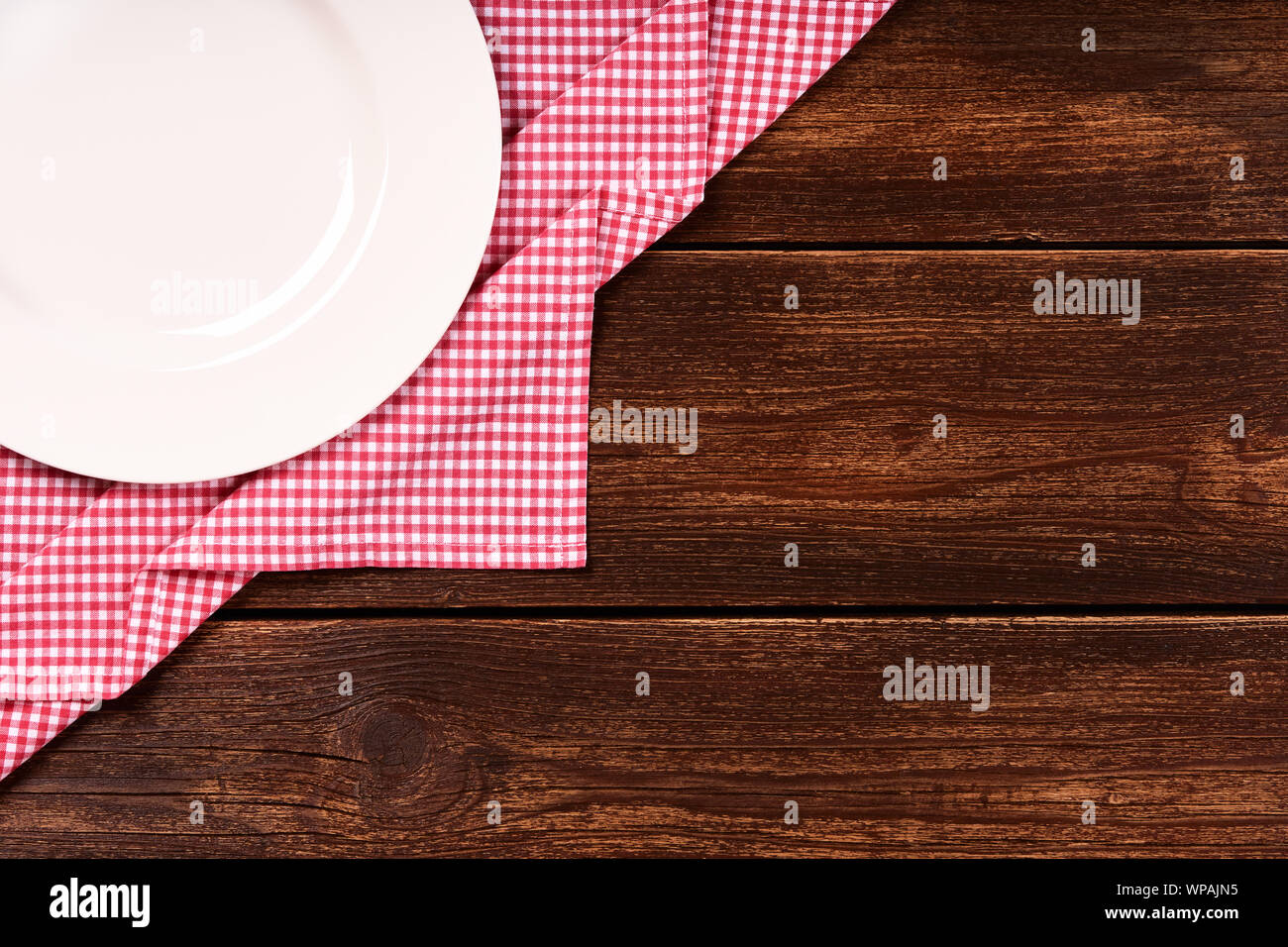 Sentar plana de madera antigua con fondo rojo a cuadros trapo de cocina, placa blanca redonda y espacio para el texto. Foto de stock