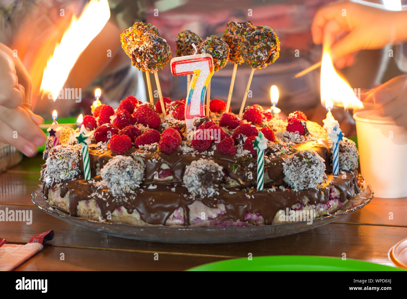 Prender fuego a las velas en una tarta de cumpleaños para niños, manos con la quema de coincidencias en bokeh. Foto de stock