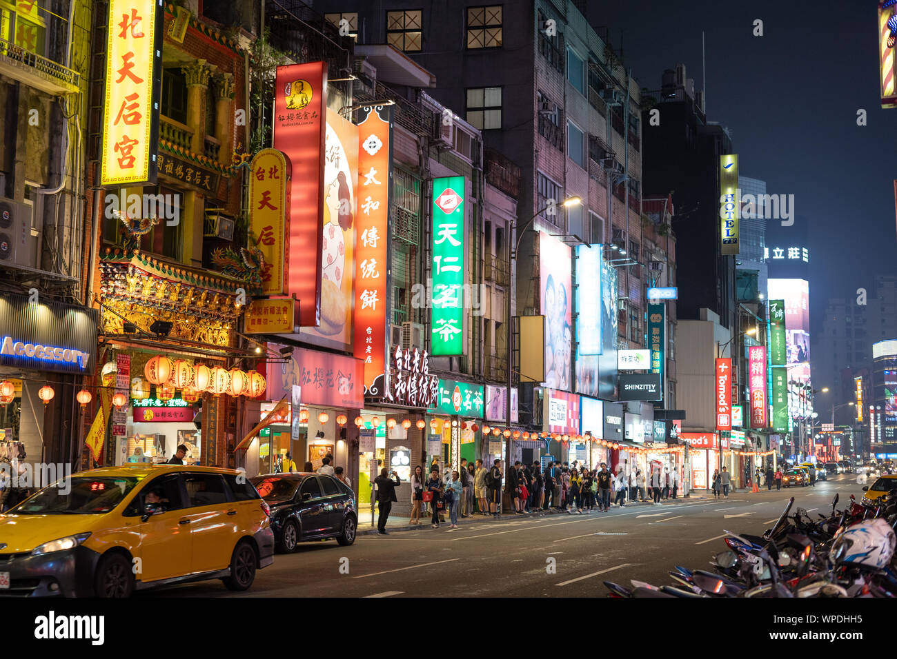 Taipei, Taiwán: vacía la calle urbana en la noche iluminada por los colores de la publicidad de neón con caracteres chinos. La gente esperando el autobús, taxi por conducción. Foto de stock