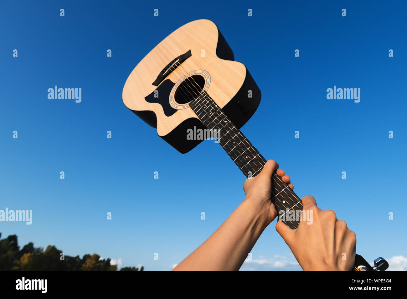 Madera en guitarra acústica amarilla chica manos contra el cielo azul, en la puesta de sol. Hermosa música de fondo. Día soleado. Foto de stock