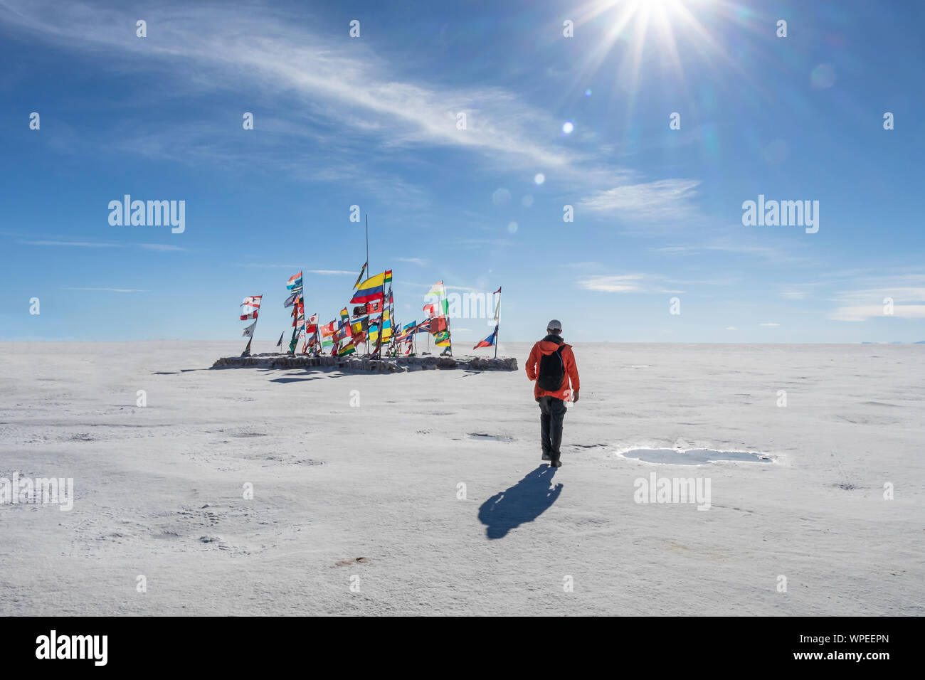 Joven caminando hacia las banderas internacionales de diferentes países en el Salar de Uyuni en día soleado con rayos de sol, Bolivia, South America Travel voc Foto de stock