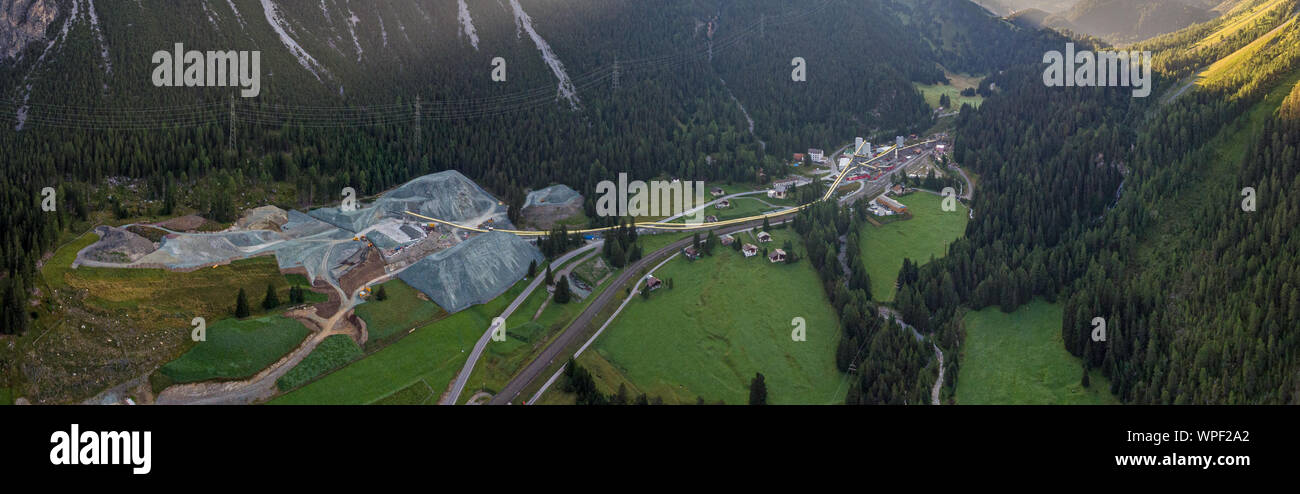 Antena drone opiniones de una construcción a gran escala situado en un exuberante y verde valle alpino y los picos de los alrededores de bañarse en el sol. Foto de stock