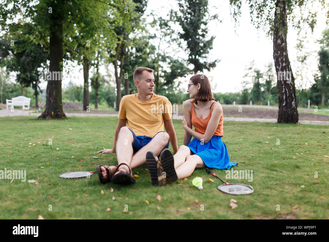 Pareja milenaria sentados en el césped después de jugar al bádminton en el parque Foto de stock