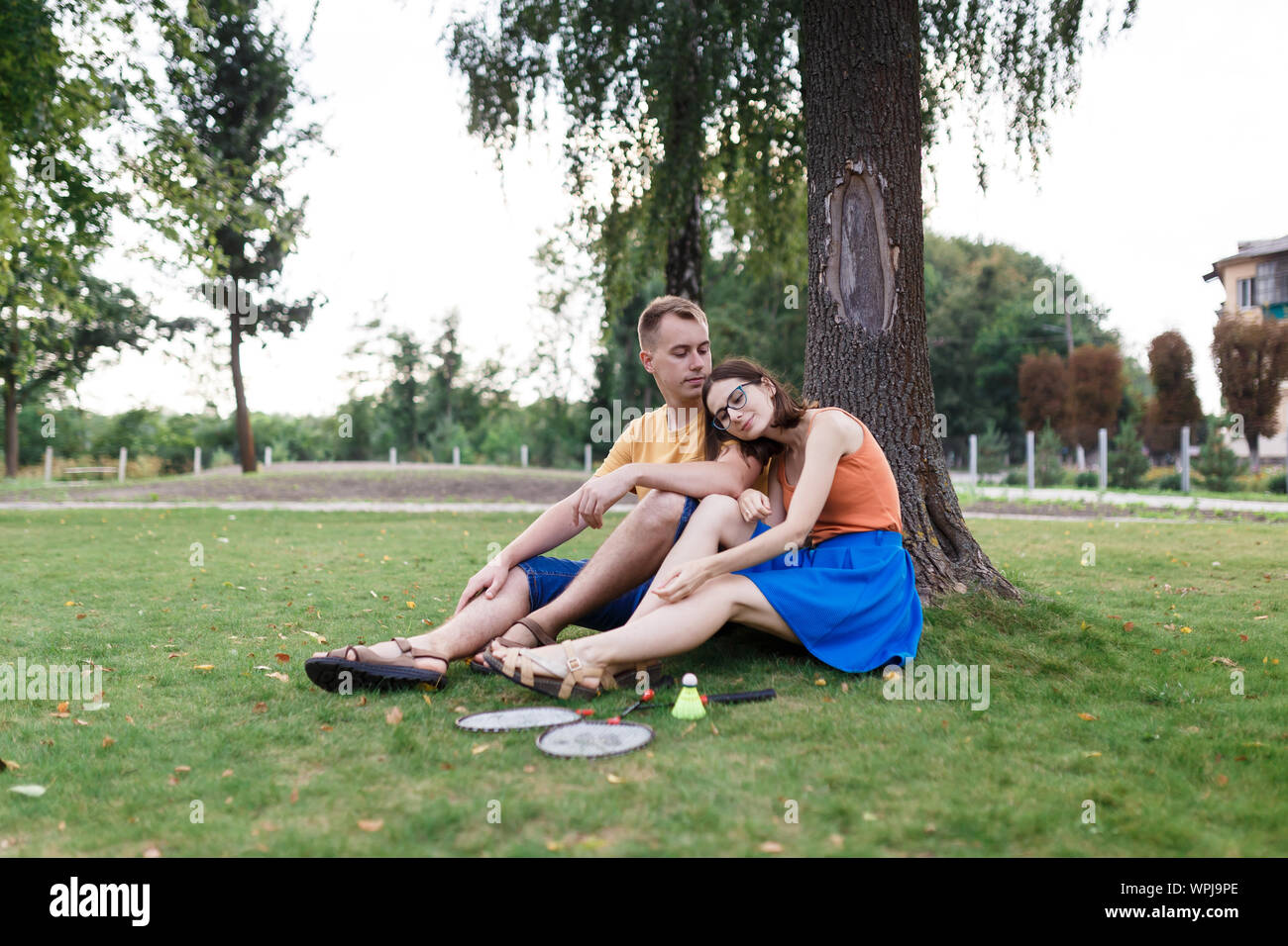 Pareja milenaria sentados en el césped después de jugar al bádminton en el parque Foto de stock