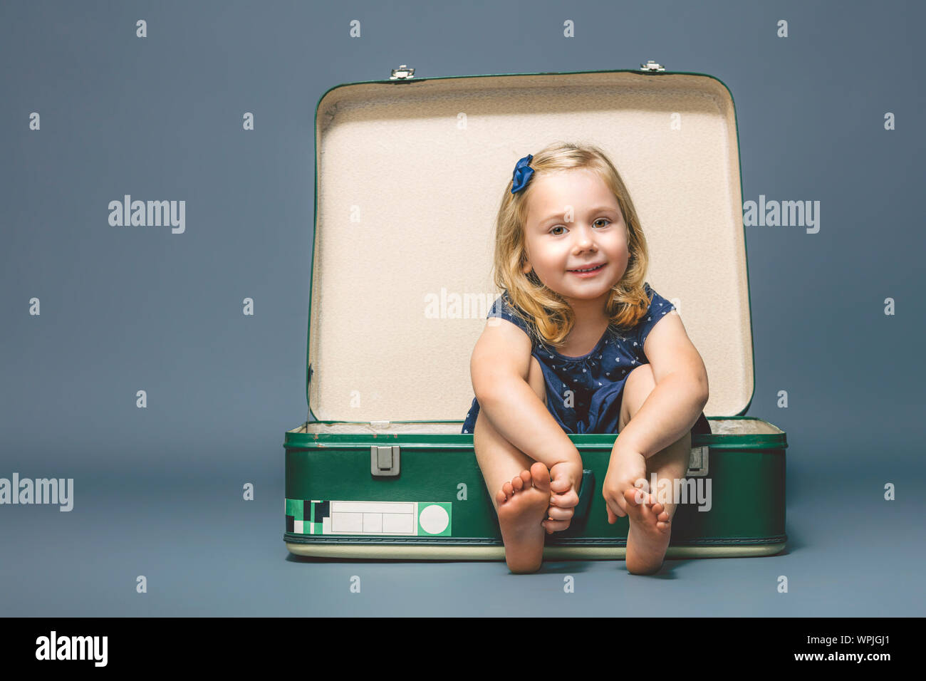 Retrato de una niña de 3 años de edad descalzo sentado dentro de una vieja maleta. toma en el estudio. Foto de stock