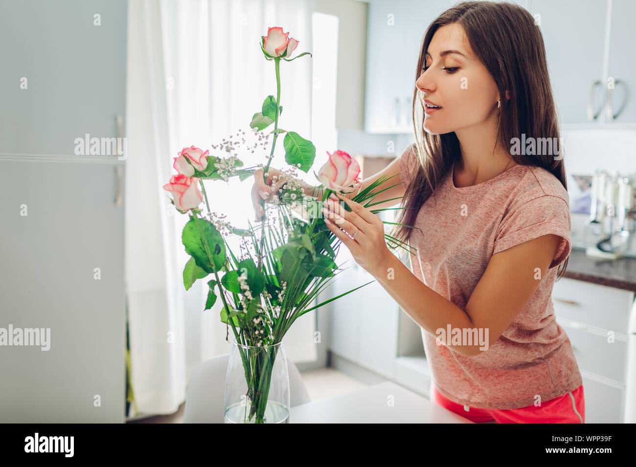 Mujer se pone las rosas en florero. Ama de casa joven teniendo cuidado de  calidez en la cocina decorando con flores Fotografía de stock - Alamy