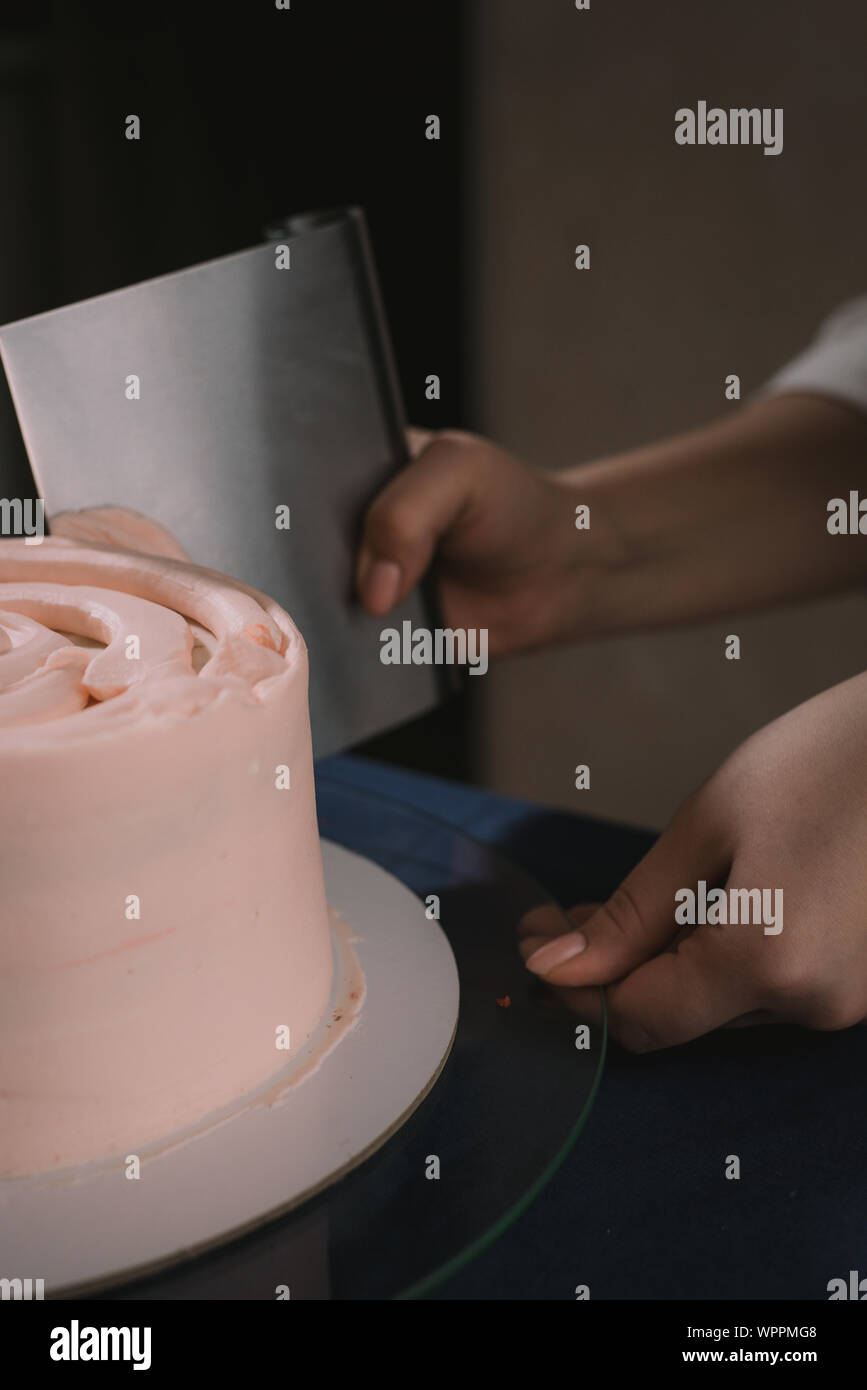 Pastelería alinea la crema con una espátula. El maestro de pasteles de crema en líneas beige pastel de boda Foto de stock