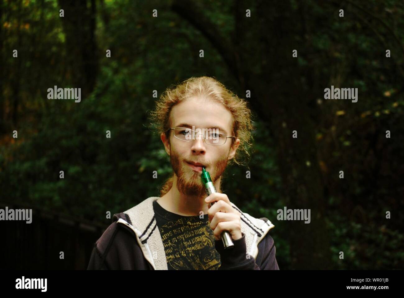 Retrato de Joven fumar cigarrillo electrónico mientras está de pie contra árboles Foto de stock