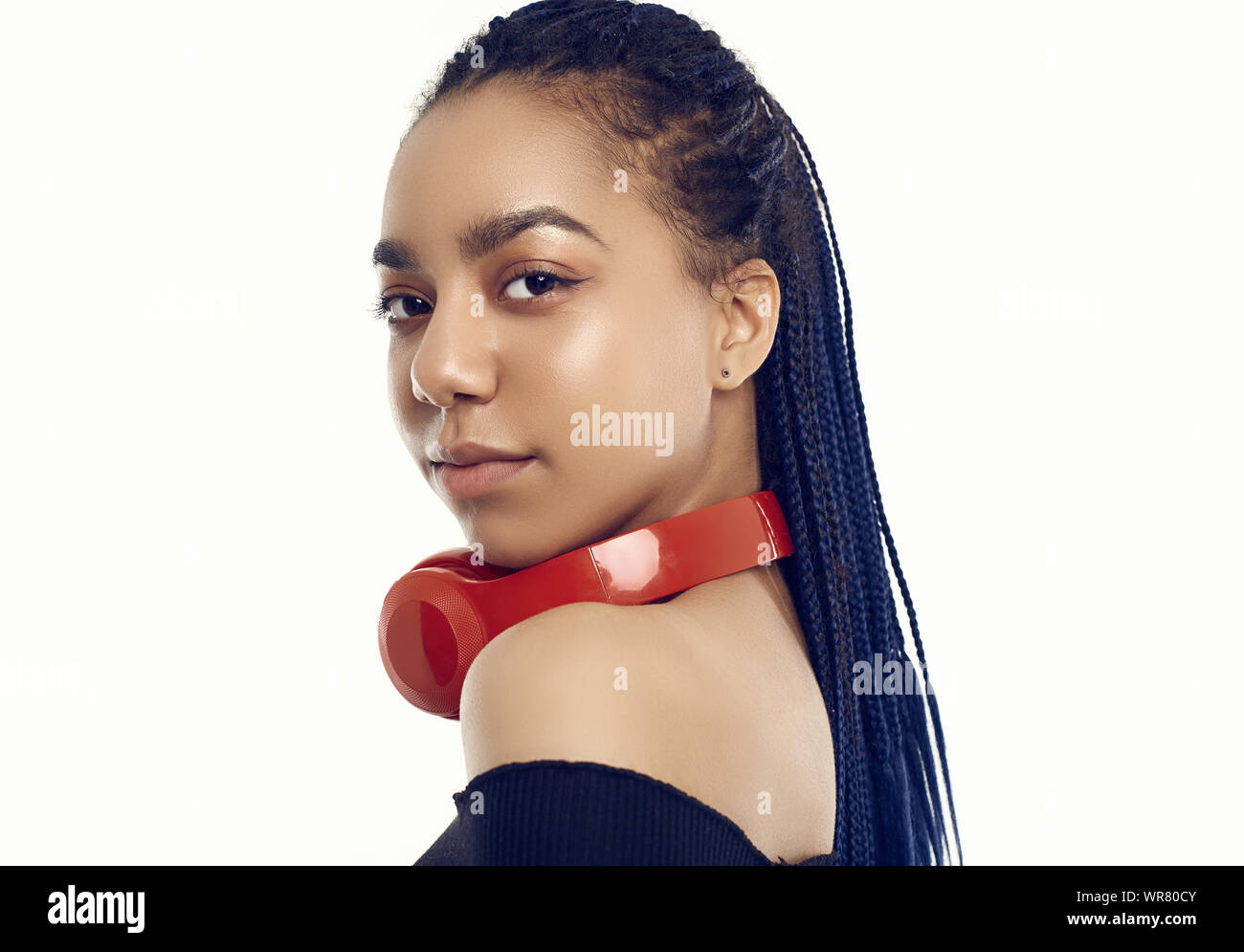 Retrato de hermosa morena africana adolescente con dreadlocks escuchando música a través de auriculares inalámbricos aislado sobre fondo studio Foto de stock