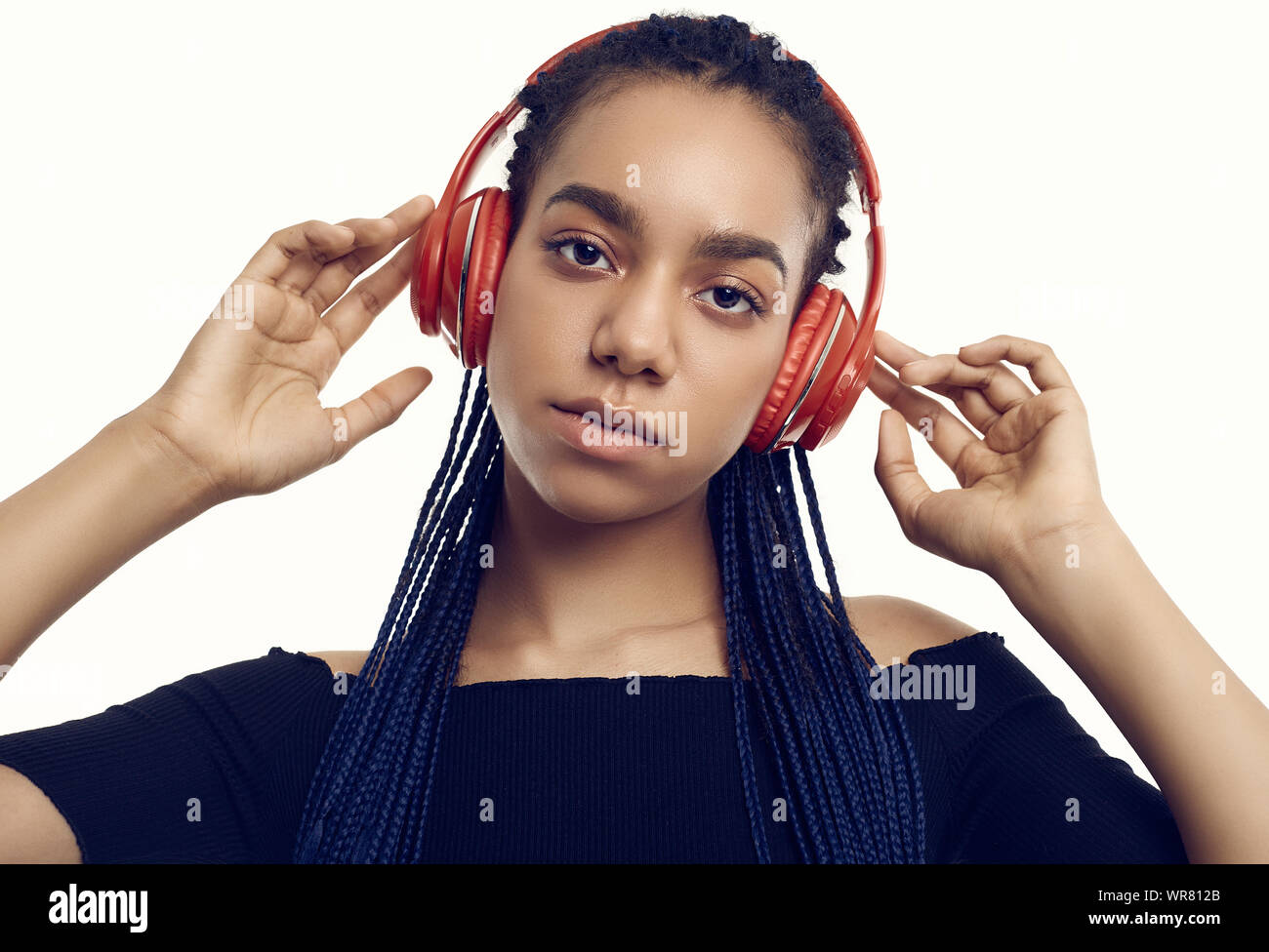Retrato de hermosa morena africana adolescente con dreadlocks escuchando música a través de auriculares inalámbricos aislado sobre fondo studio Foto de stock